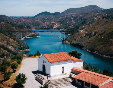 Capela no cimo de um monte com um rio e uma ponte ao fundo