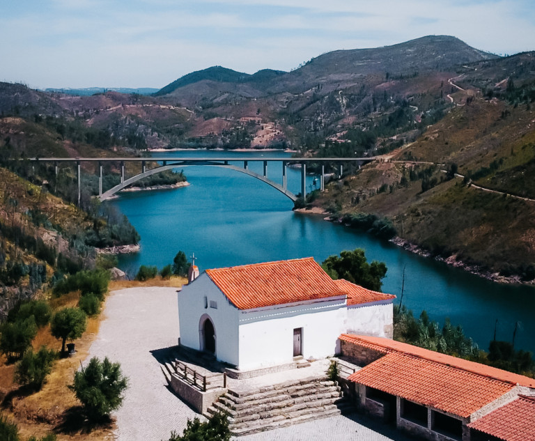 Capela no cimo de um monte com um rio e uma ponte ao fundo